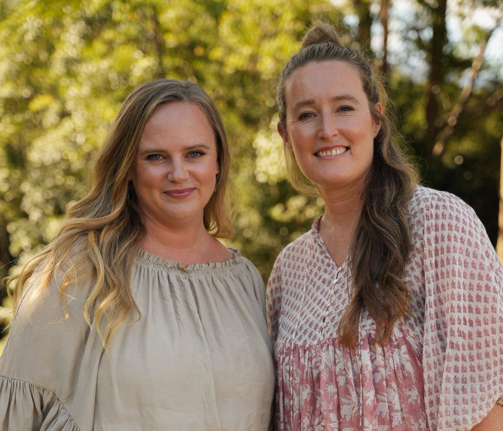 Two women standing outdoors with a blurred natural background