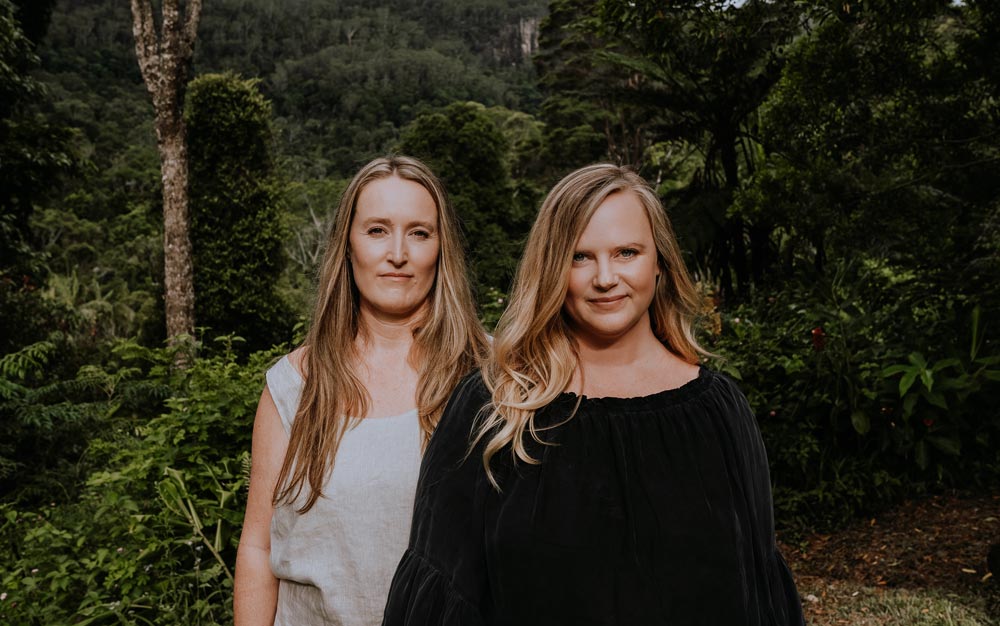 The Reconnected's founders, Eleanor and Emma, standing side-by-side and smiling in a lush tropical setting
