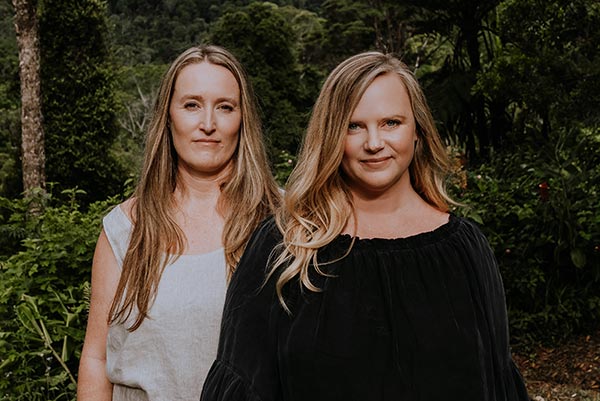 Eleanor and Emma standing side-by-side and smiling in a lush tropical setting