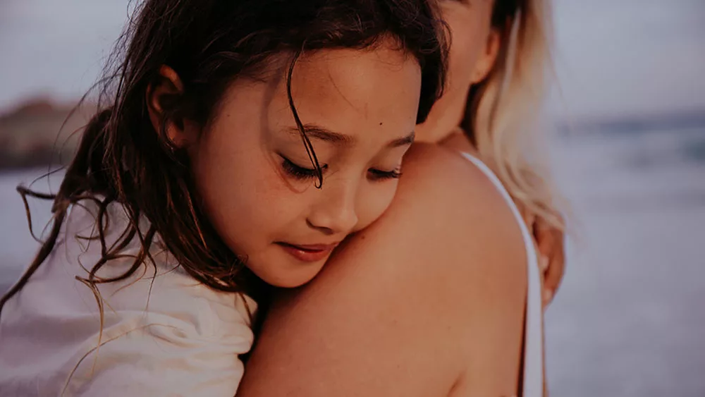 A girl in her mothers arms, slumped over her shoulder, looking sad