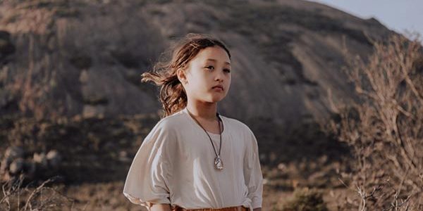 A sensitive child standing in front of a desert mountain with a gentle stare